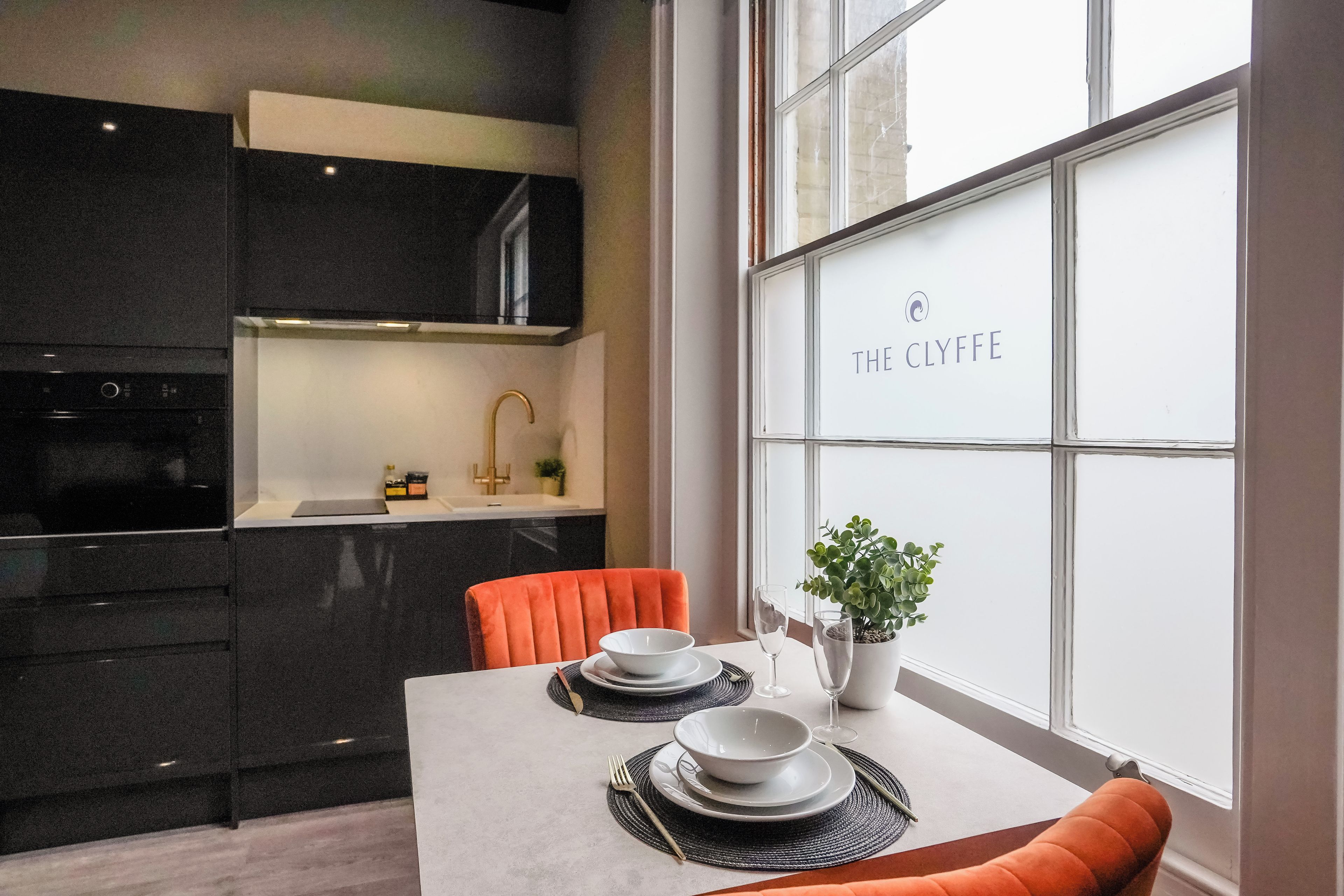 Een moderne keuken met donkere kastjes, een witte aanrecht en een eethoek met een tafel voor twee personen.