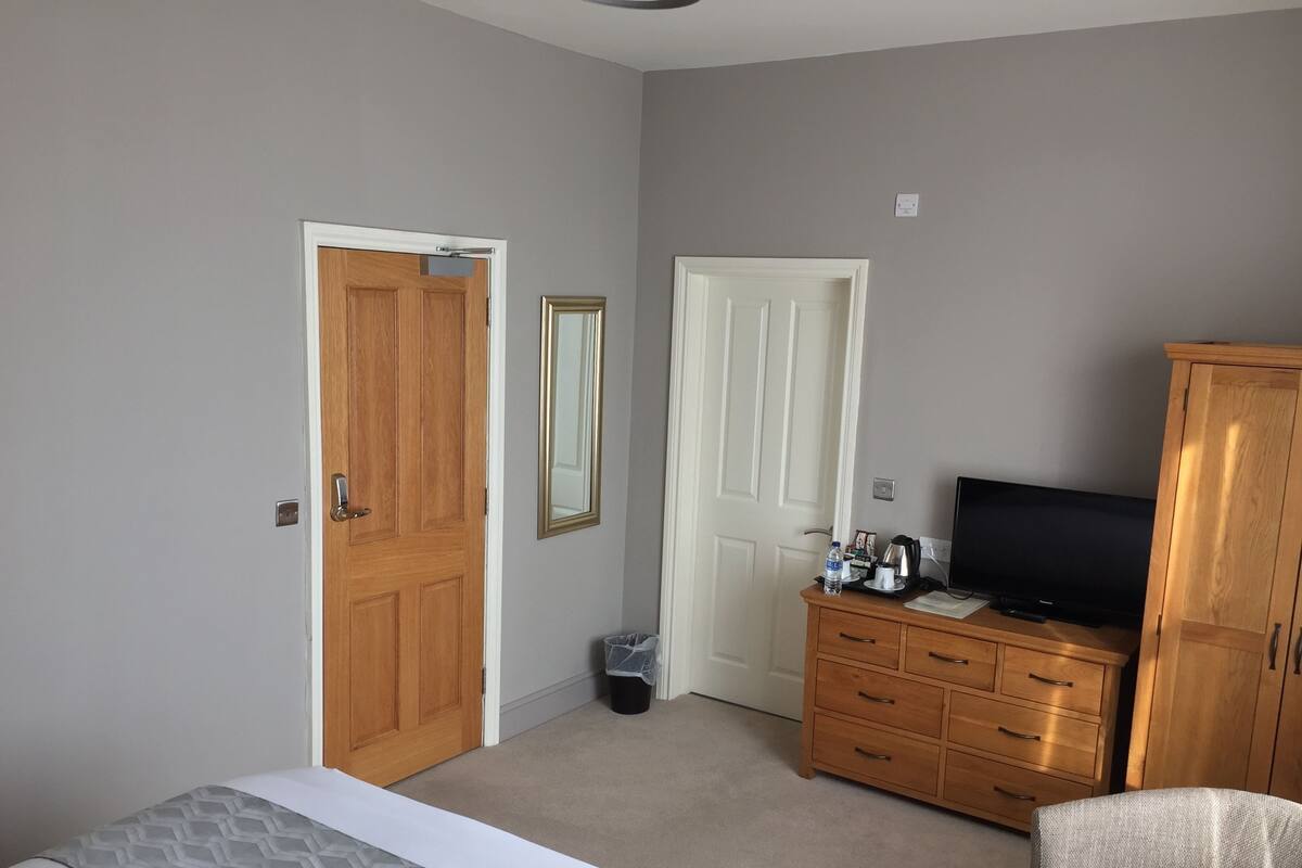 A hotel room with a bed, a wooden wardrobe, a television, and a chair.