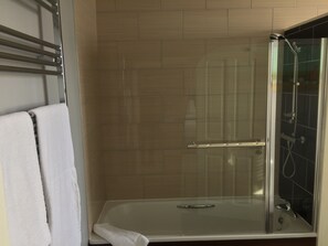Un baño moderno con ducha de vidrio, una toalla blanca en el suelo y pared con azulejos.
