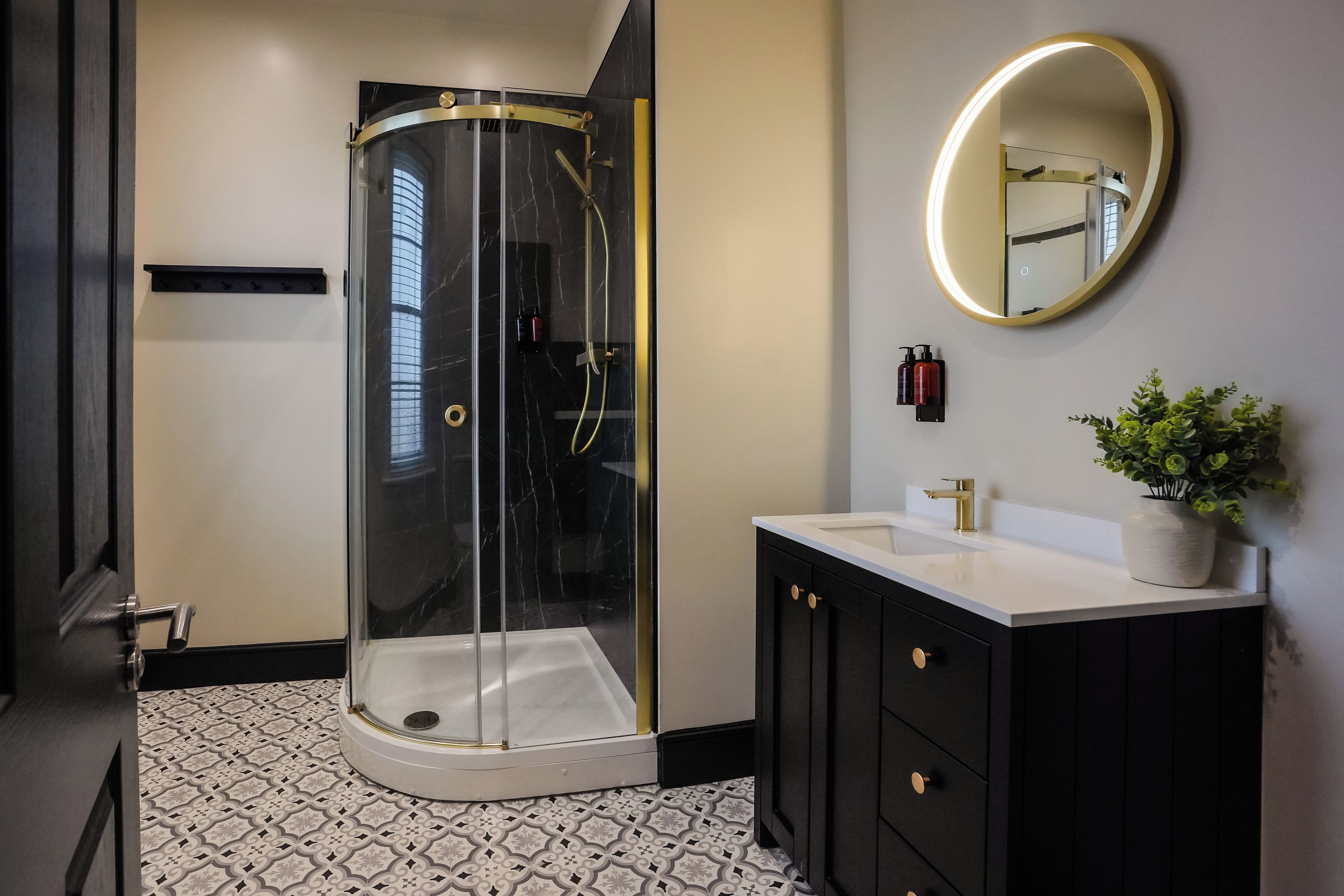 Ein modernes Badezimmer mit einer Glaskabine zur Dusche, einem weißen Waschbecken, einem schwarzen Waschtisch und einem runden Spiegel.