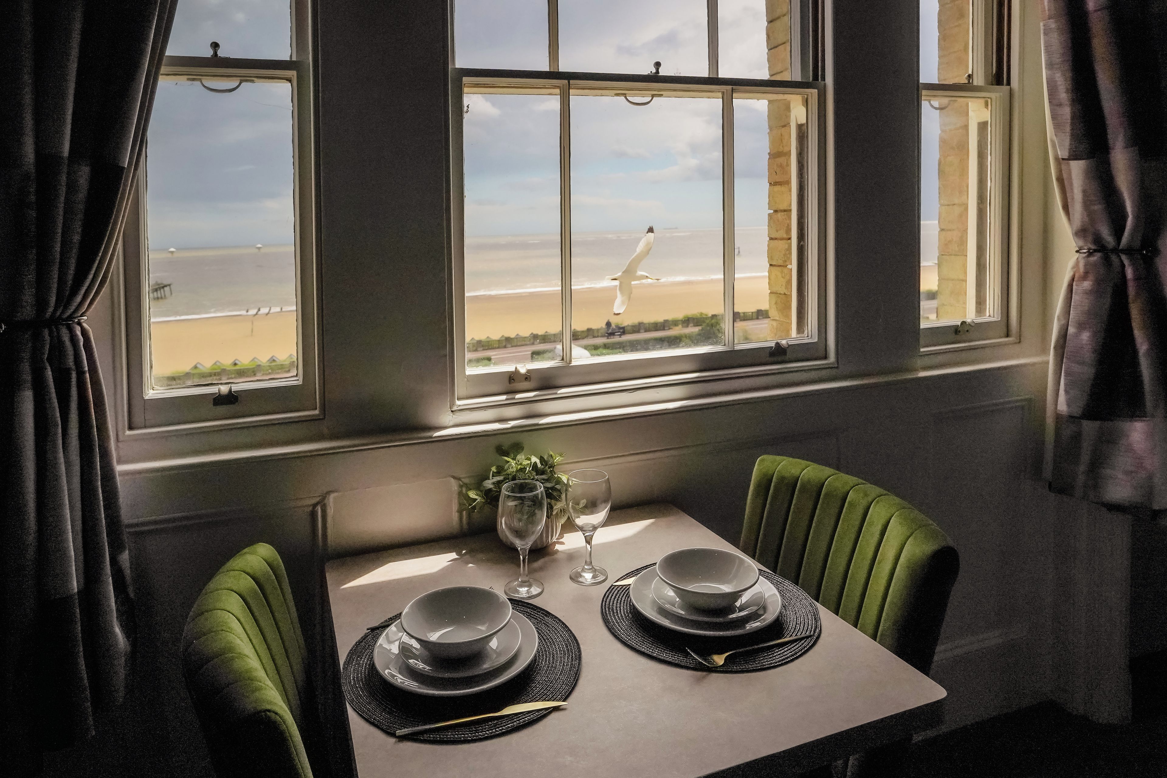 Une table à manger avec deux assiettes et un verre, placée devant une fenêtre donnant sur une plage.