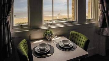Une table à manger avec deux assiettes et un verre, placée devant une fenêtre donnant sur une plage.