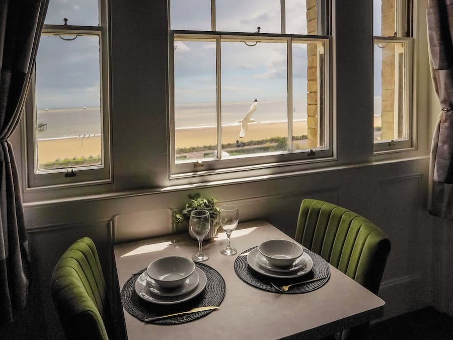 Une table à manger avec deux assiettes et un verre, placée devant une fenêtre donnant sur une plage.