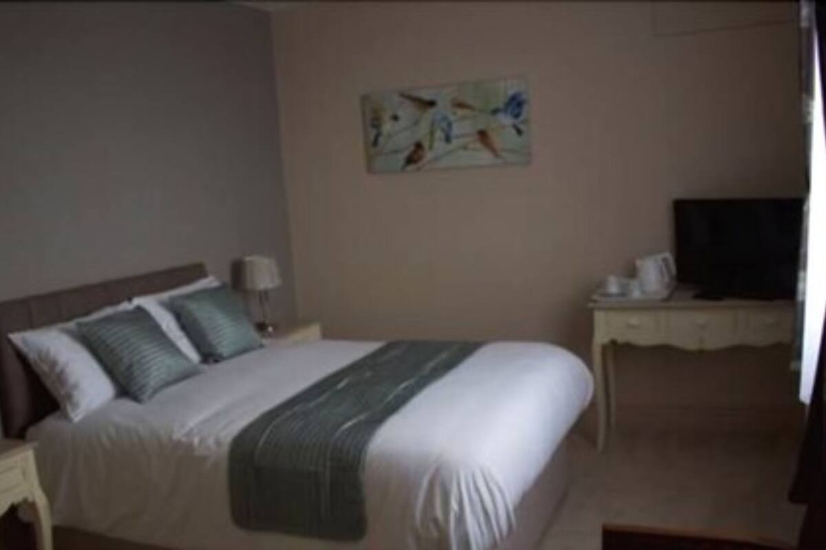 A bedroom with a bed, a desk, a chair, a lamp, and a painting on the wall.