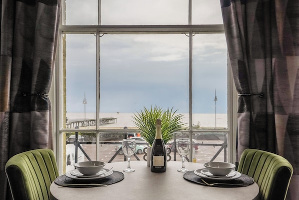 Una mesa de comedor con una botella y copas, con vista a una playa y un muelle.
