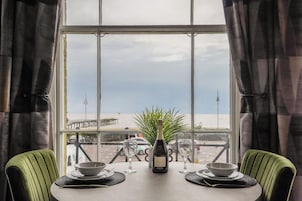 Una mesa de comedor con una botella y copas, con vista a una playa y un muelle.
