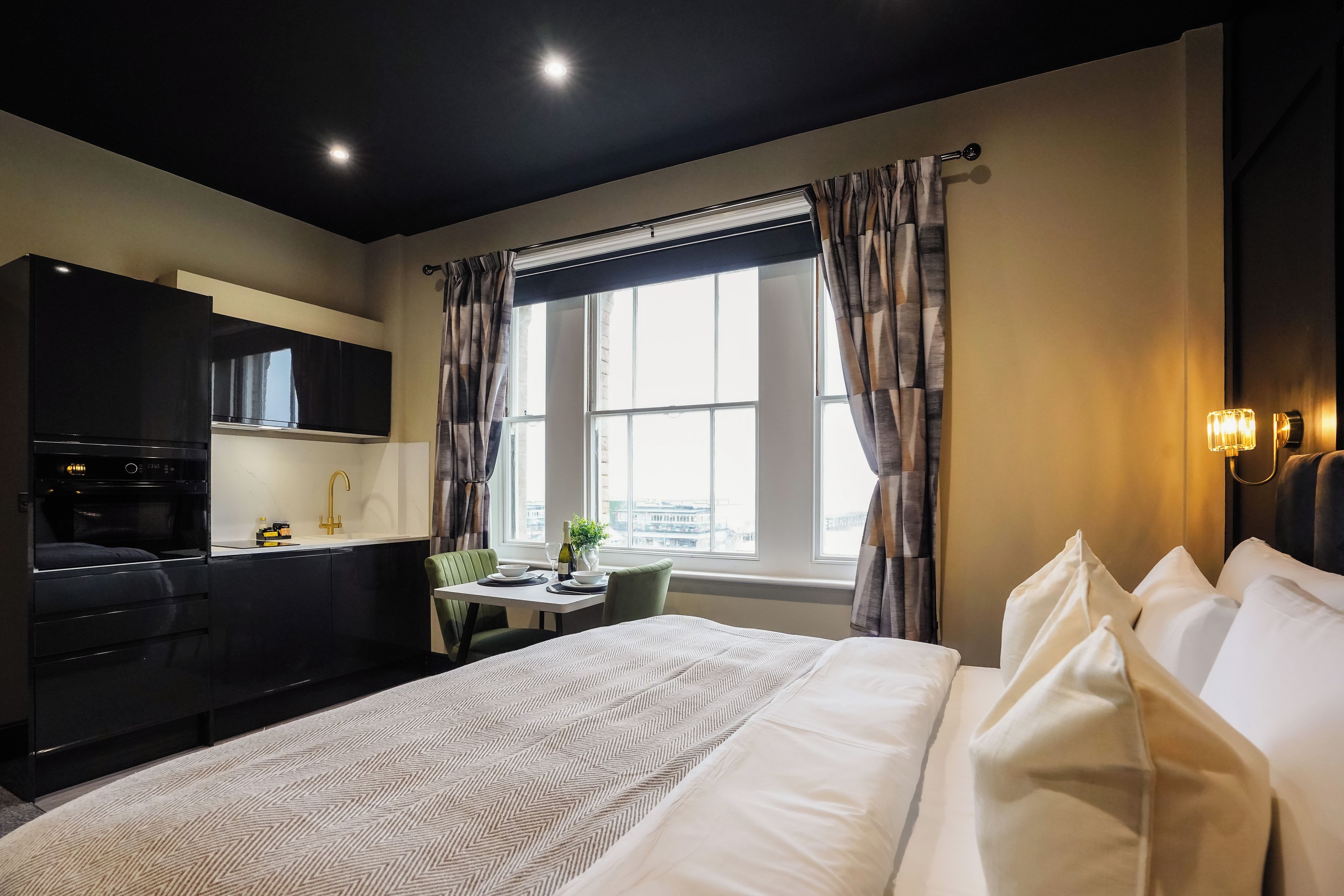 Een moderne hotelkamer met een bed, een zithoek, een kitchenette en grote ramen.