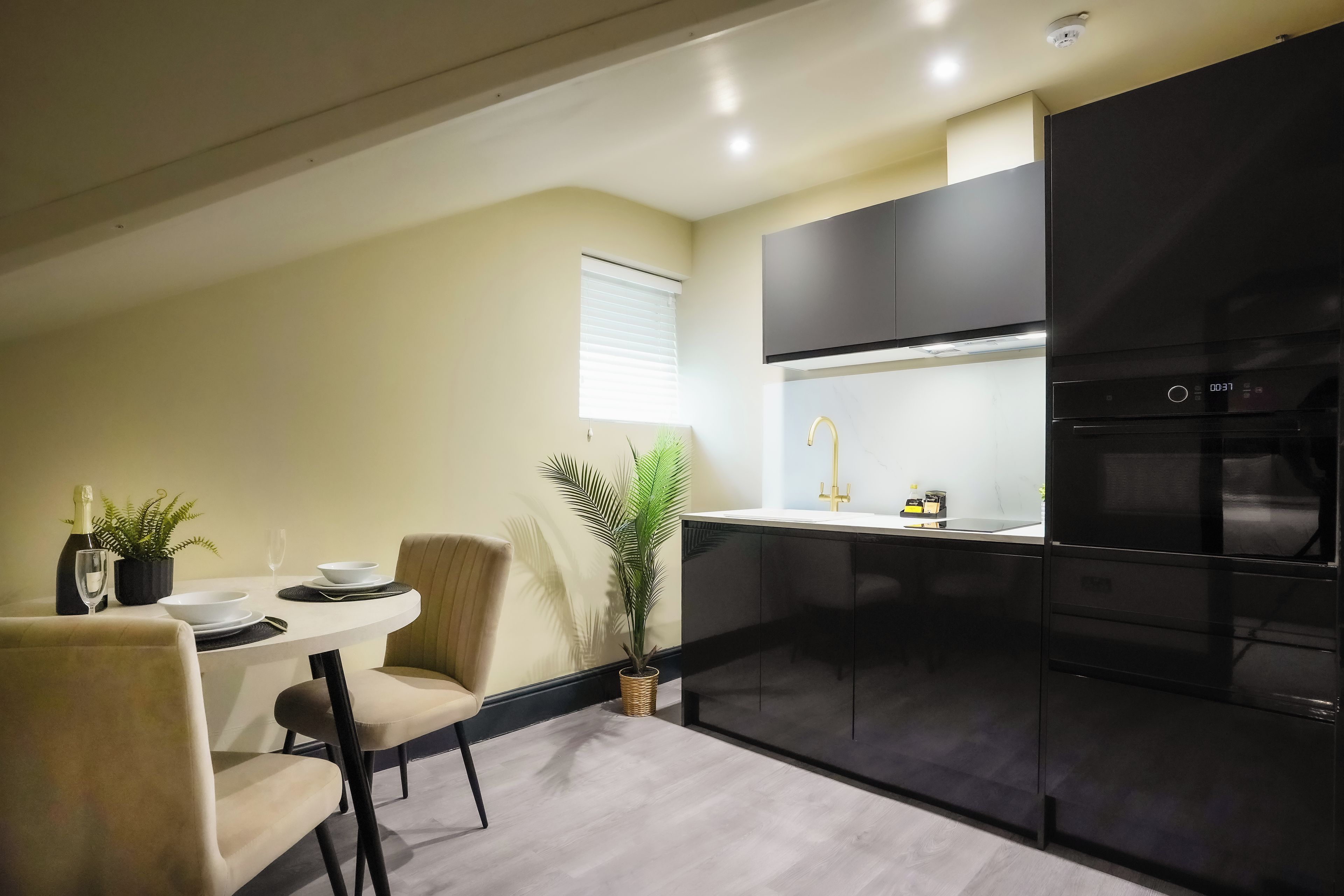 A modern kitchen with black cabinetry, a stainless steel refrigerator, and a dining area with a table set for two.