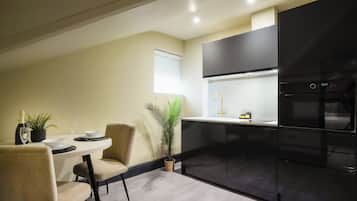A modern kitchen with black cabinetry, a stainless steel refrigerator, and a dining area with a table set for two.