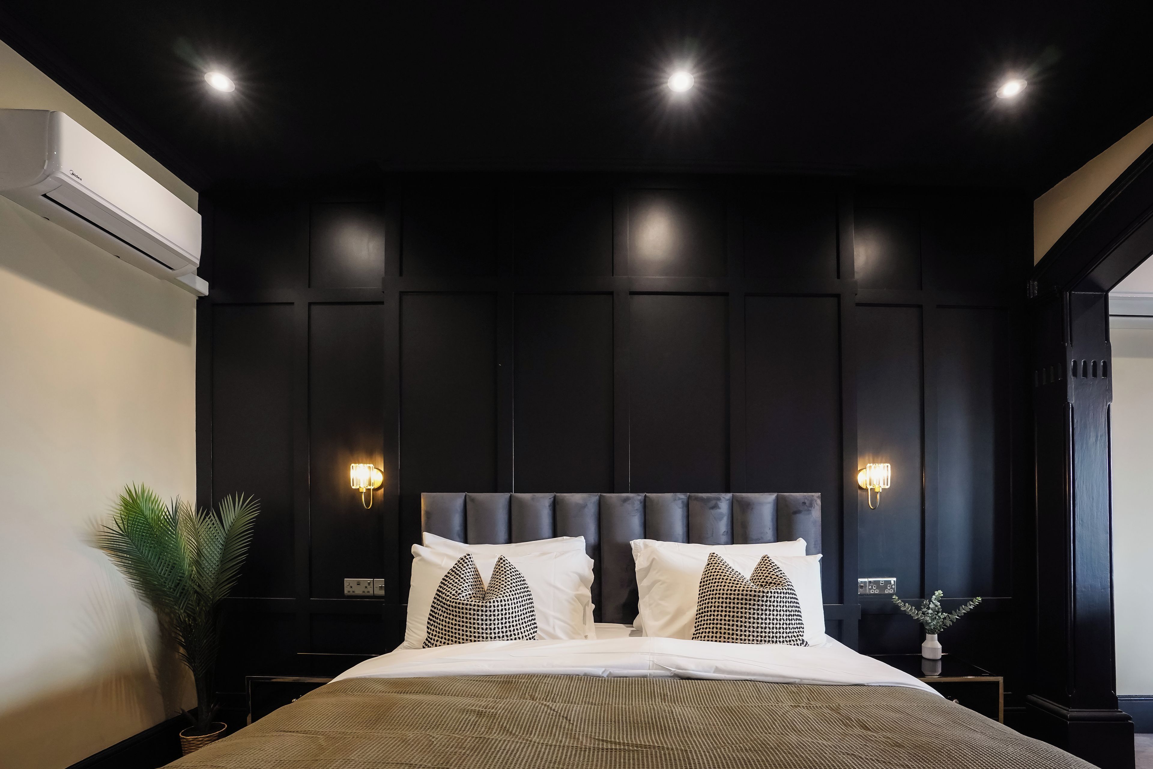 Ein Schlafzimmer mit Wandverkleidung aus dunklem Holz, einem gepolsterten Kopfteil und zwei Nachttischlampen.