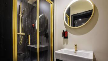 A bathroom with a glass-enclosed shower, a white sink, and a round mirror with a gold frame.