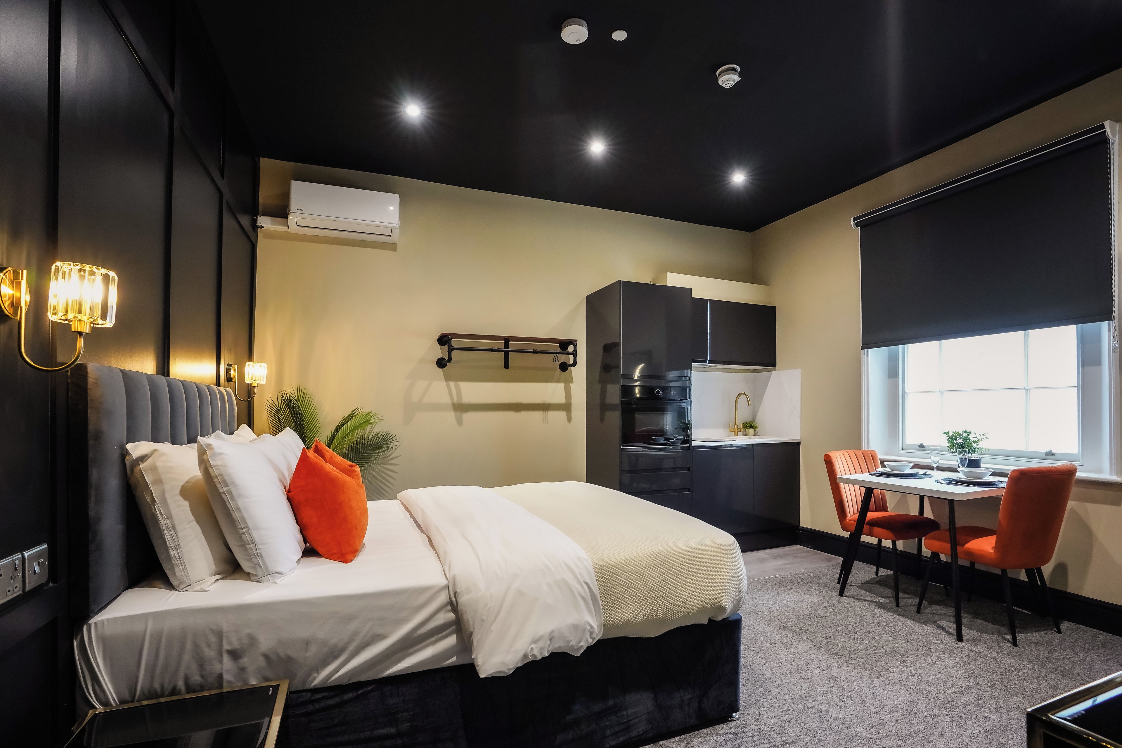 A modern hotel room with a bed, bedside table, and a small kitchenette.
