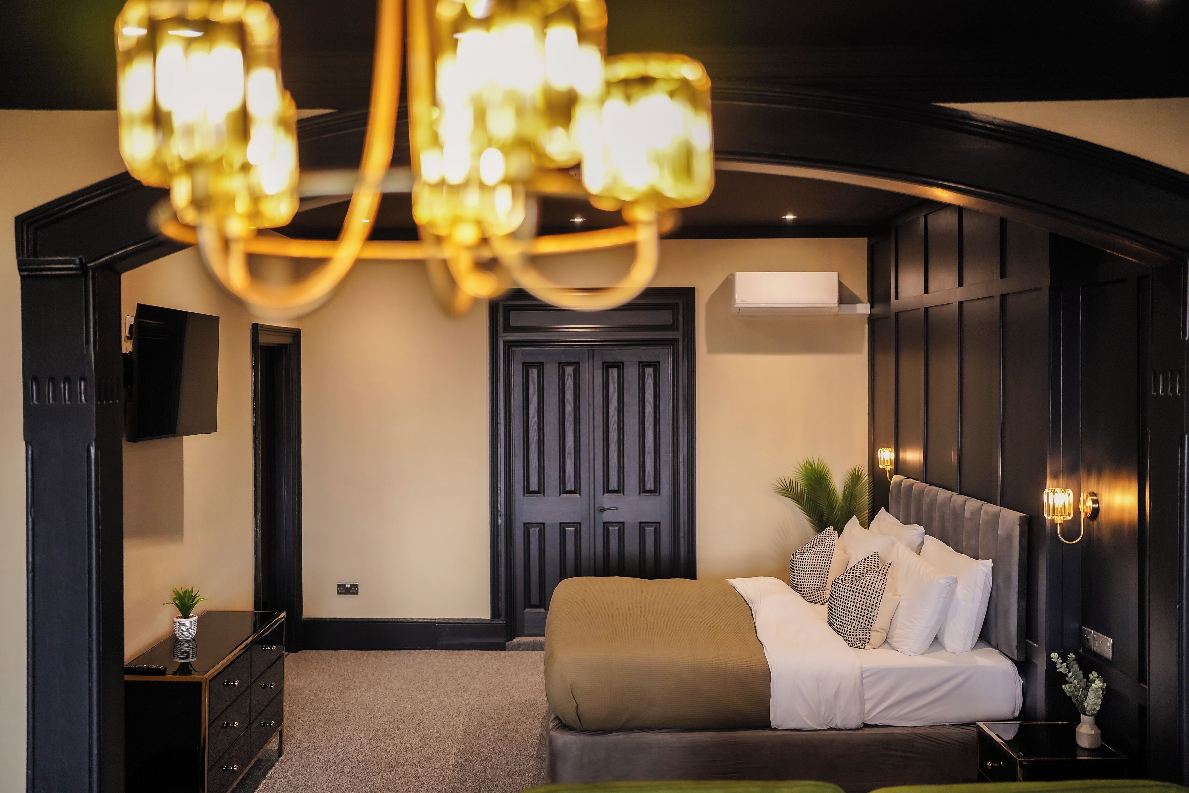 Une chambre à coucher moderne avec un lit, une commode, un téléviseur et un lustre.
