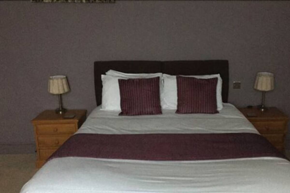 A neatly made bed with a dark headboard, two bedside tables with lamps, and a dark wall.