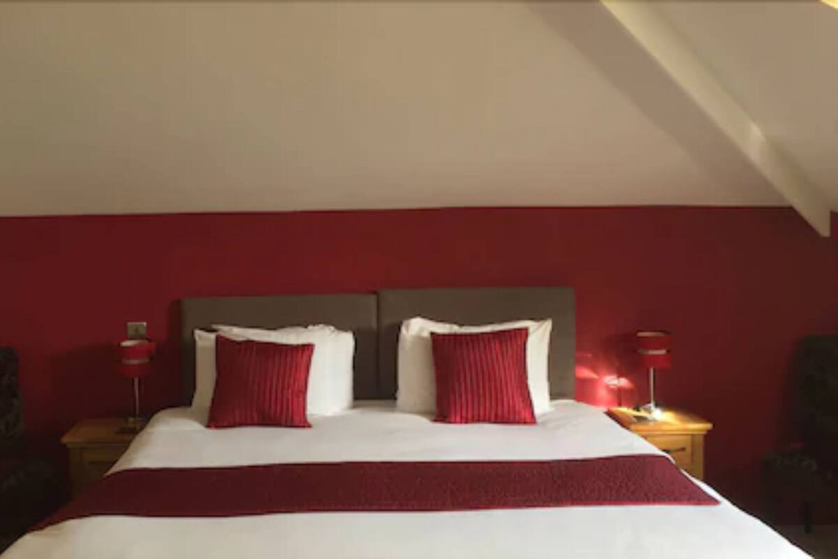 A hotel room with a large bed, red walls, and two bedside tables with lamps.