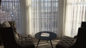 Una habitación con un ventanal grande, dos sillones tapizados y una pequeña mesa redonda con papeles.