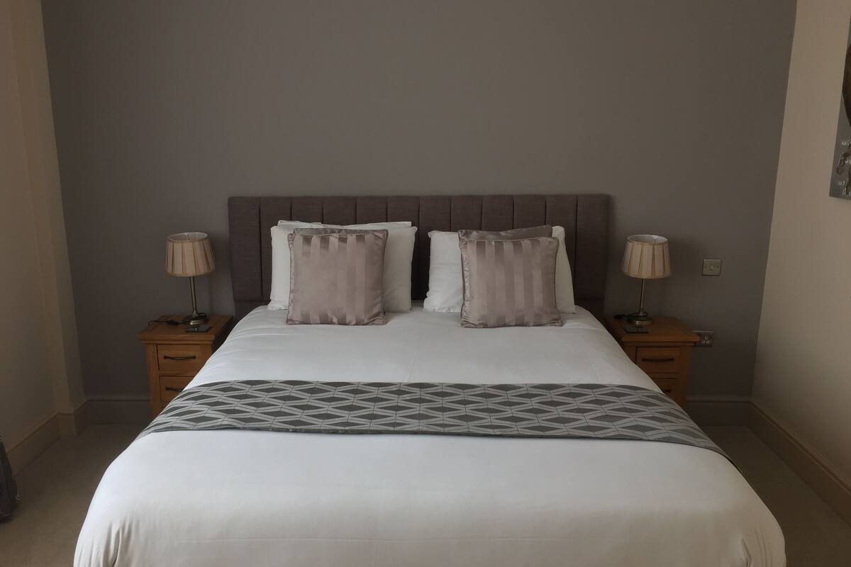 A neatly made bed with a geometric-patterned bedspread, two bedside tables with lamps, and a headboard with vertical panels.