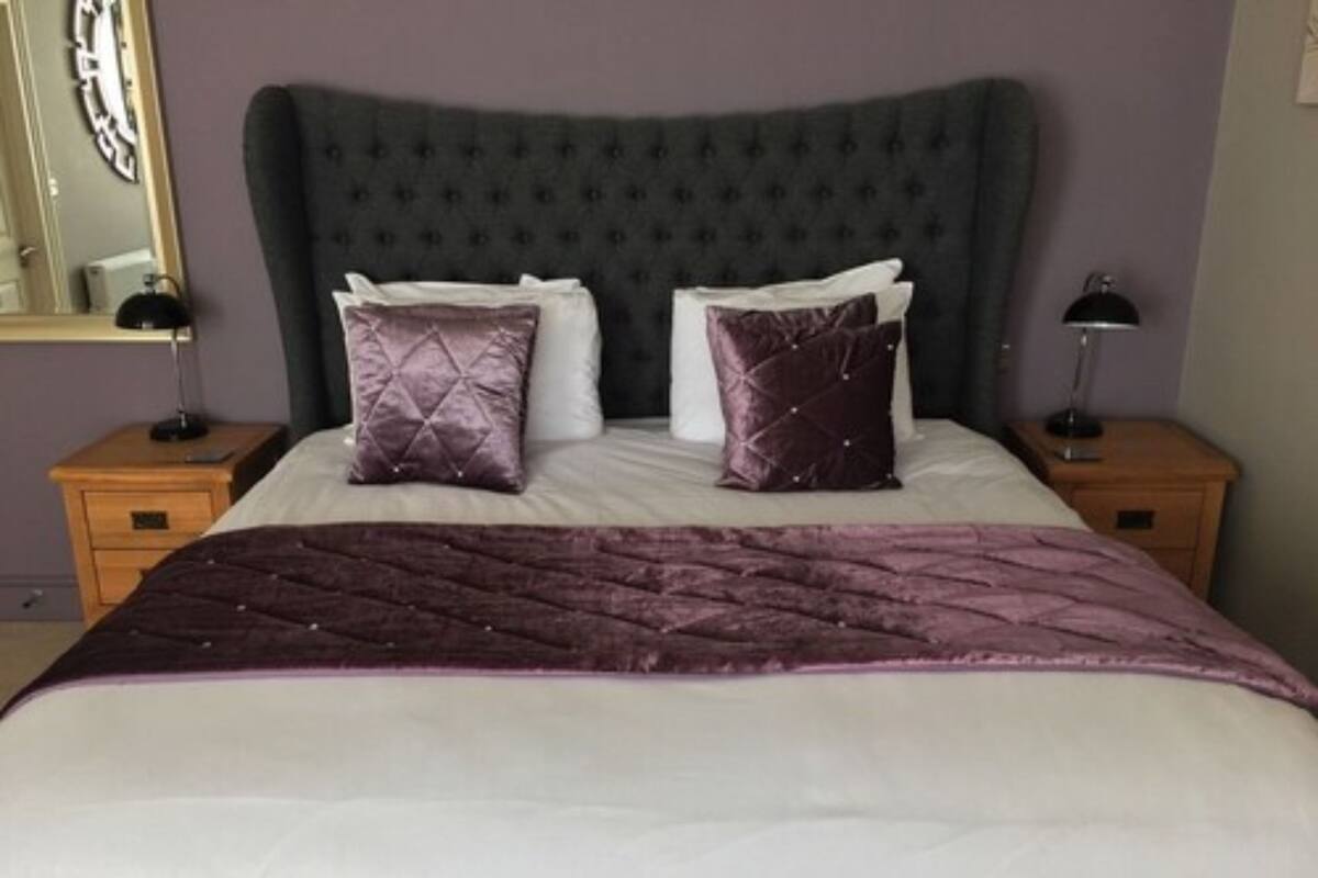 A bed with a quilted headboard, two pillows, and a bedside table with a lamp.