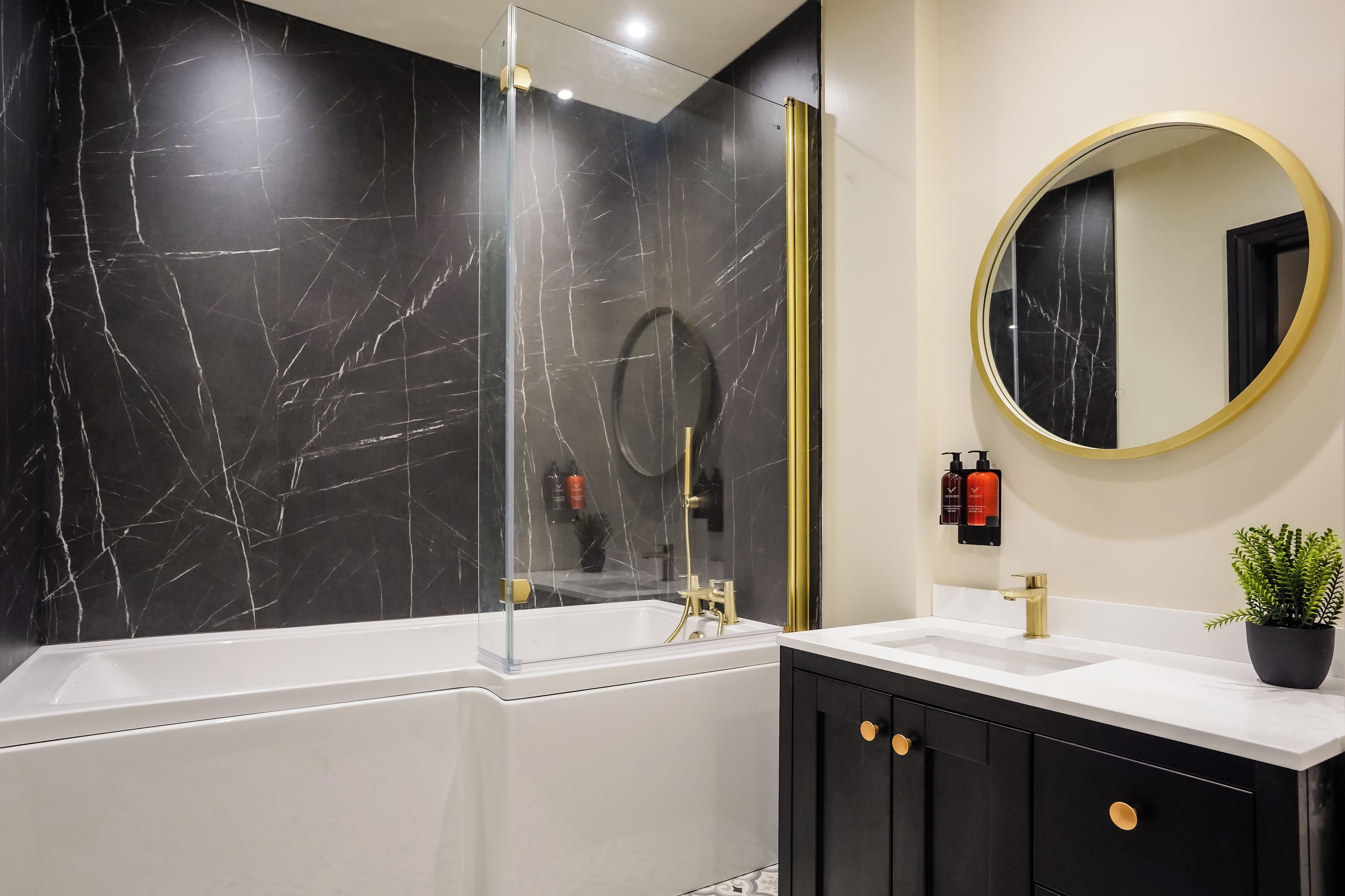 Un baño moderno con una bañera, un espejo redondo y una pared de mármol negro.