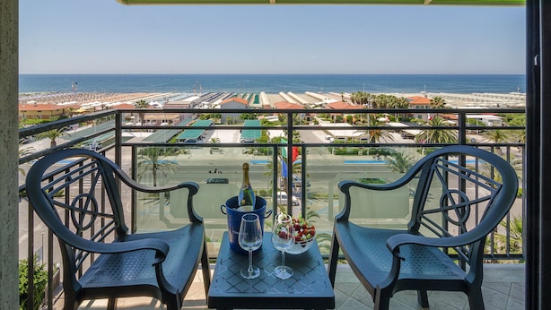 A balcony with two chairs and a table, overlooking a beach and a parking lot. - Hotel Siesta (Camaiore)