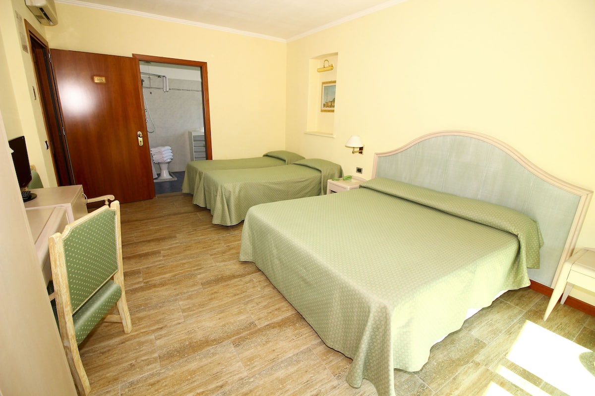 A hotel room with two single beds, a wooden chair, a desk, and a bathroom visible through an open door.