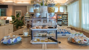 A buffet setup with various food items, including pastries, fruits, and beverages, arranged on a counter with a decorative plant and a coffee machine. - Hotel Siesta (Camaiore)