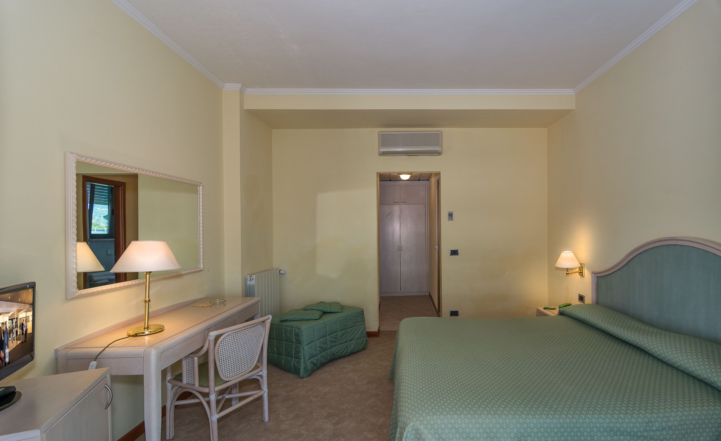 Een hotelkamer met een bureau, stoel, bed en spiegel.