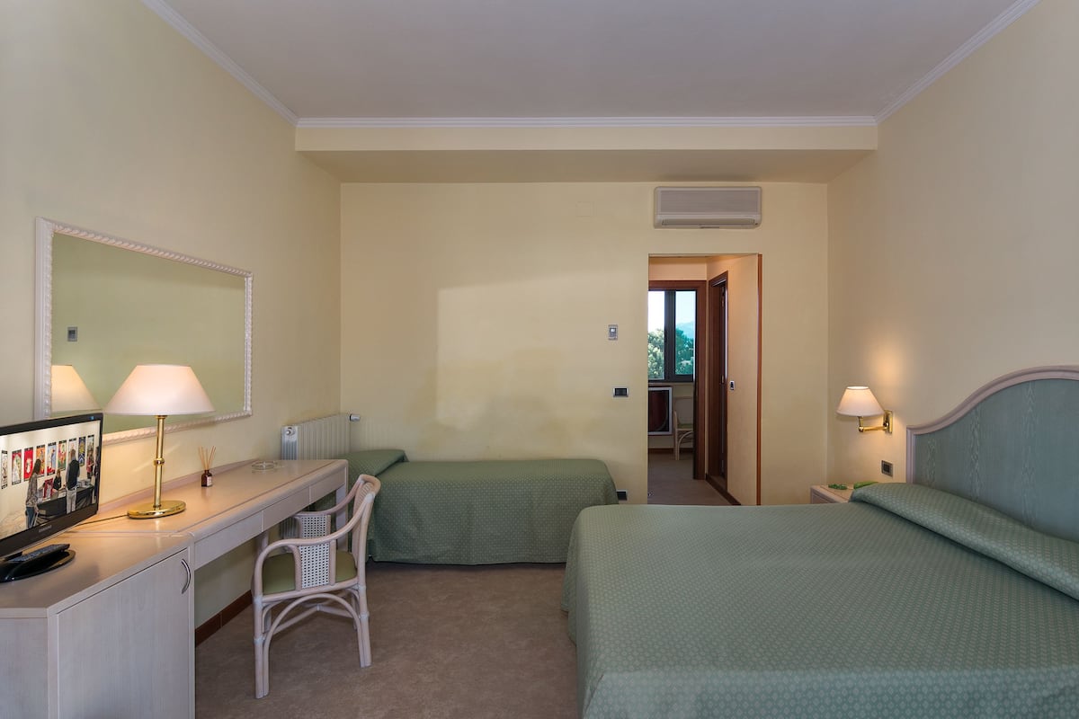 A hotel room with two single beds, a desk with a lamp, a chair, and a large mirror.