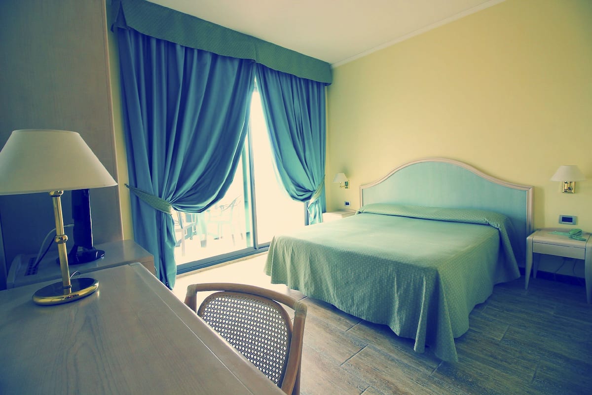 A hotel room with a bed, a desk, a chair, and a window with curtains.