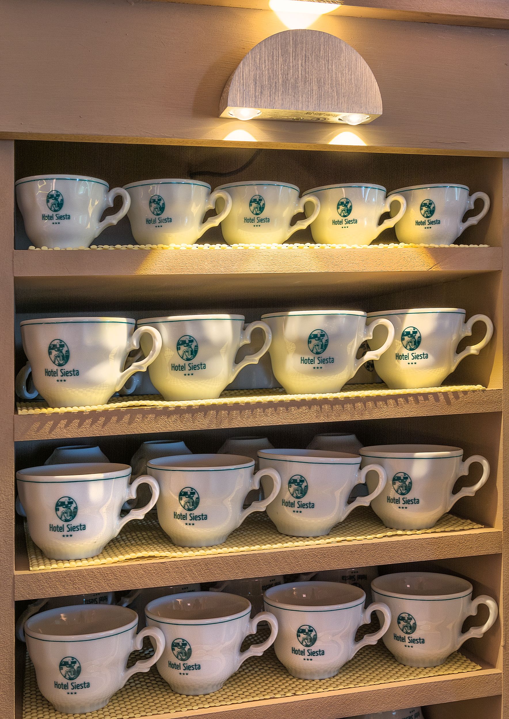 Estanterías con tazas y platillos blancos con la etiqueta 'Hotel Siesta'.
