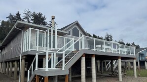 A waterfront house with a glass deck, concrete pillars, and a covered outdoor area. - Lovely Beachfront Home with Amazing Views! (Netarts)