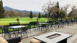 Un espace extérieur aménagé avec des tables et des chaises, un foyer et une vue sur un terrain de golf et des montagnes.