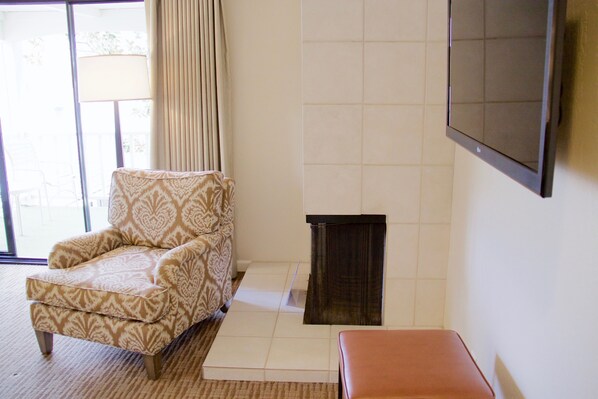 A room with a patterned armchair, a fireplace, and a television mounted on the wall.