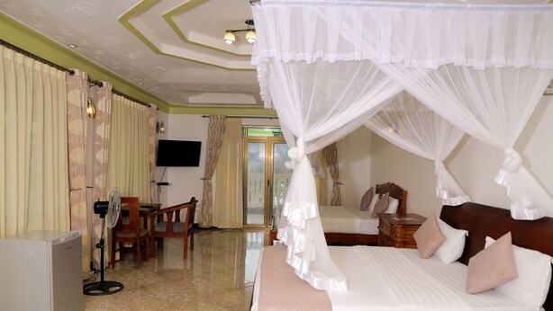 Una habitación de hotel con cama con dosel, televisor montado en la pared, escritorio con silla y minibar.
