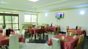 Un comedor con mesas cubiertas por manteles rojos, sillas y un televisor montado en la pared.