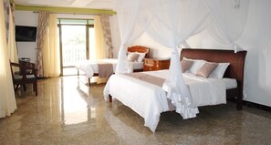 A hotel room with two beds, a wooden headboard, a TV, and a desk. - Victoria Royal Beach Hotel (Entebbe)