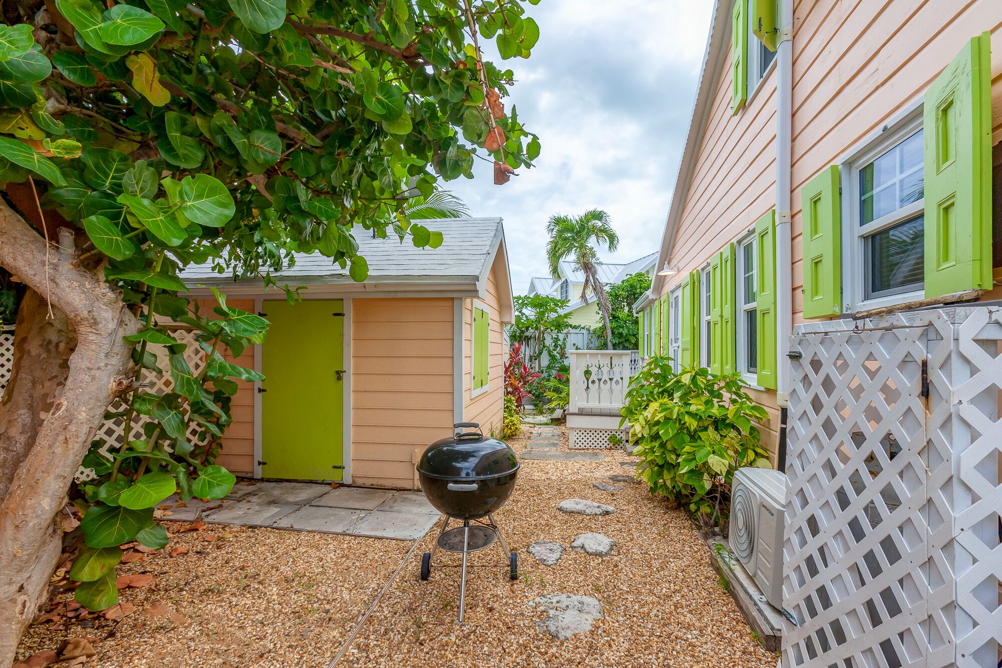 A narrow pathway leading to a building with a green door and a barbecue grill in the foreground.