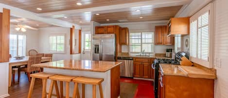 A spacious kitchen with wooden cabinets, a large island with stools, a refrigerator, stove, and a microwave.