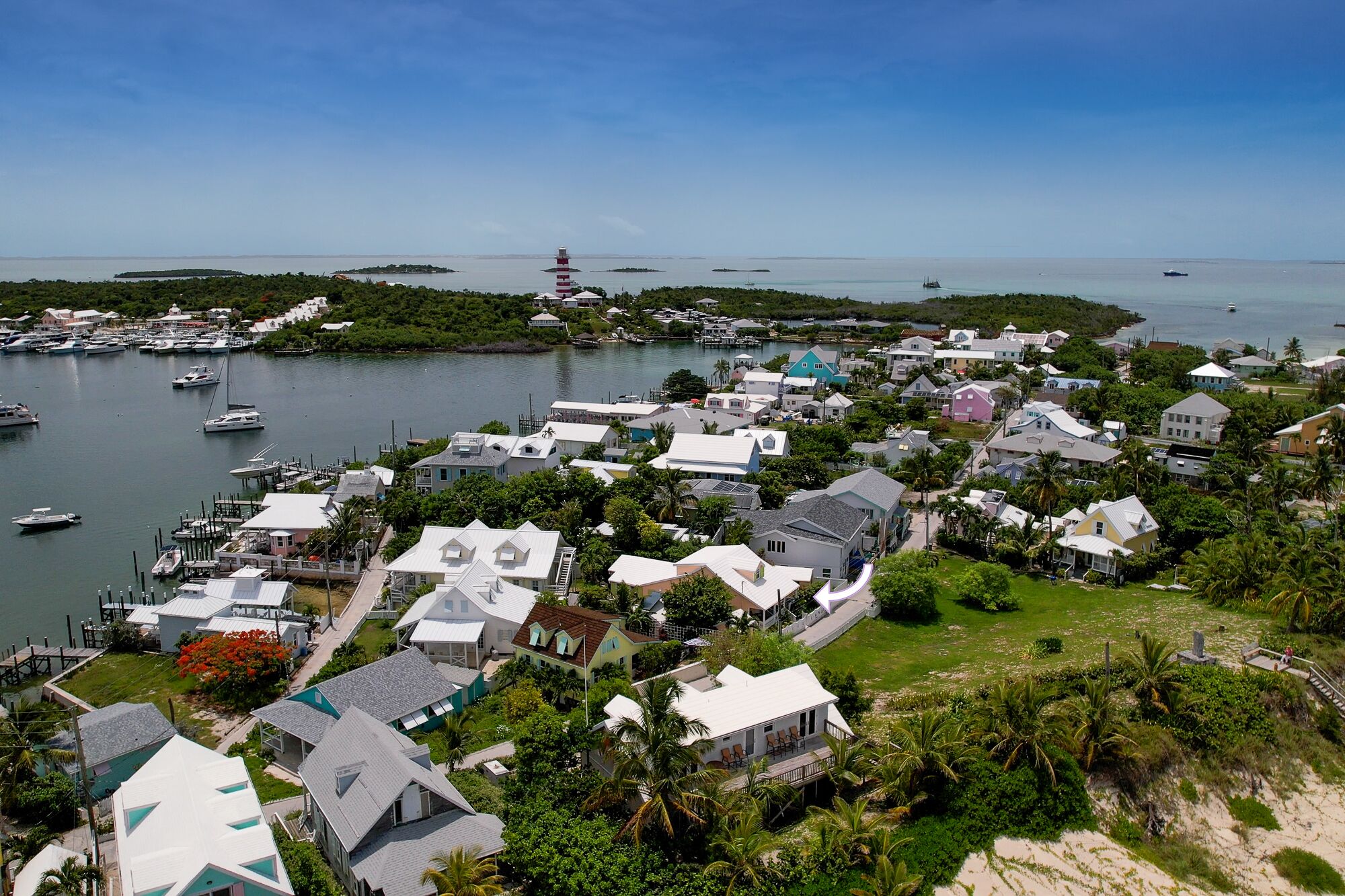 An aerial view of a coastal town with houses, a lighthouse, and boats.