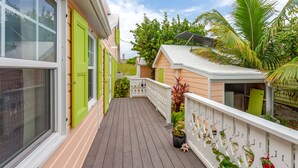 A wooden deck with a white railing, a small shed, and lush greenery. - Green Shutters: Charming 19th-Century Cottage in the Heart of Hope Town (Elbow Cay)