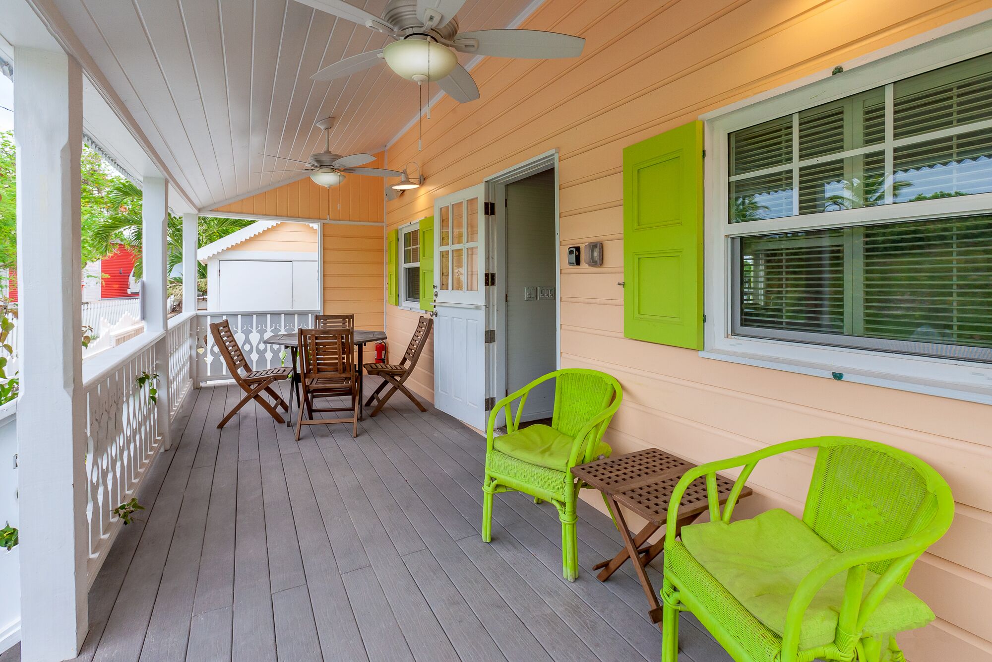 A covered porch with a table and chairs, a ceiling fan, and a window with shutters.