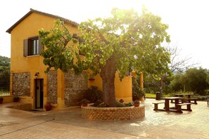 Un edificio amarillo de fachada de piedra, un árbol en el centro y mesas al aire libre.