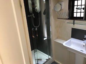 Eine begegnete Duschkabine mit Handbrause, ein Glasregal mit Spiegel und ein weißes Waschbecken mit Armatur.