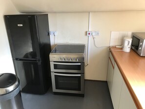 A compact kitchen with a black refrigerator, a stove with oven, and a microwave on a wooden countertop. - Pemberton House (Lincoln)
