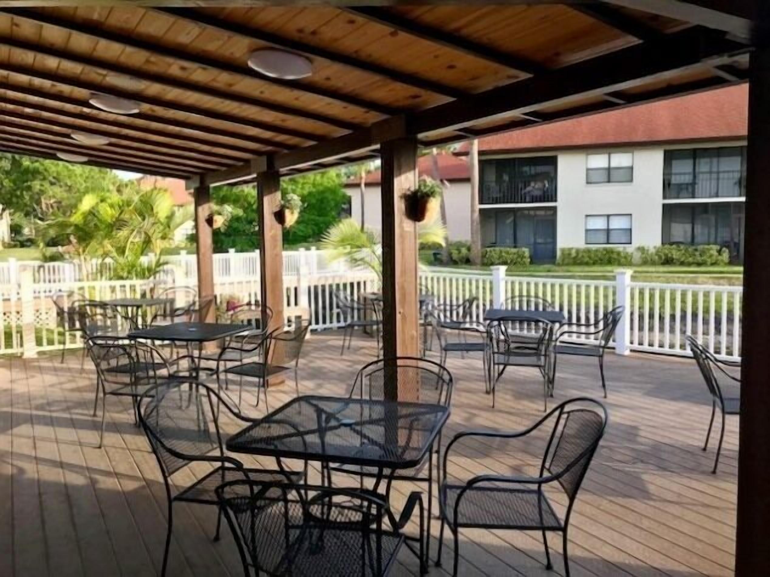 Eine Terrasse im Freien mit Tischen und Stühlen, einer Holzbeschichtung und einem weißen Zaun im Hintergrund.