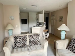 A living room with two sofas, a coffee table, and two lamps. There is a kitchen area in the background with a counter and stools. - Shorewalk 205 - Bradenton-  The Palms condo 2 Bedroom / 2 Bath,  5 miles from  Anna Maria Island and near Img, maximum occupancy of 4 people. (Bradenton)