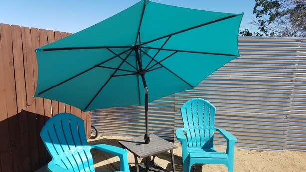 A patio with two blue chairs, a small table, and a large turquoise umbrella. - "Lucille" Vintage Glamper Hideaway (Joshua Tree)