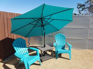 A patio with two blue chairs, a small table, and a large turquoise umbrella. - "Lucille" Vintage Glamper Hideaway (Joshua Tree)
