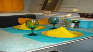A dining table with yellow plates and green wine glasses, set in a room with a window and a clock on the wall. - "Lucille" Vintage Glamper Hideaway (Joshua Tree)