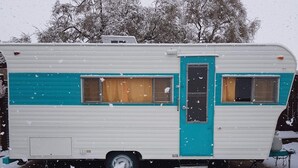 A stationary RV with a turquoise door and windows, parked in a snowy area with a picnic table nearby. - "Lucille" Vintage Glamper Hideaway (Joshua Tree)